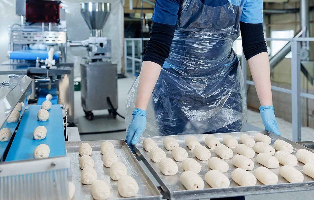 Woman picks up a metal tray with baked goods in a food production facility.