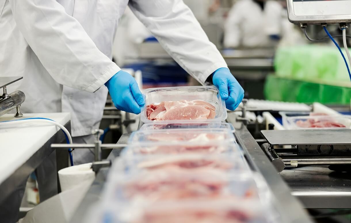 People with blue gloves and a white lab coat package a meat in a food packaging line